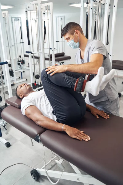 Fisioterapeuta profesional rehabilitando piernas de paciente masculino — Foto de Stock