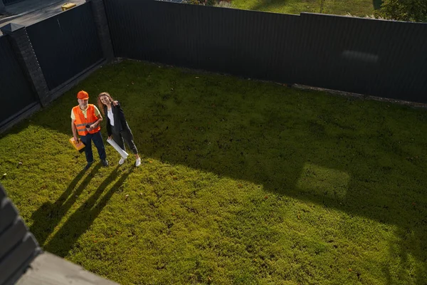 Vrouwelijke bouwkundig ingenieur met arbeider glimlachend en wijzend naar de camera — Stockfoto