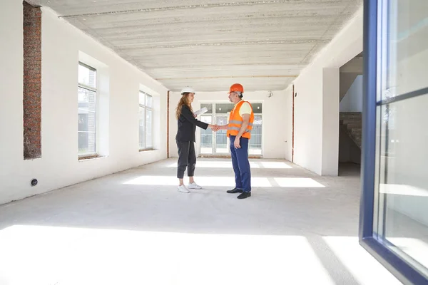 Woman construction engineer shaking hands with worker in room — Stockfoto