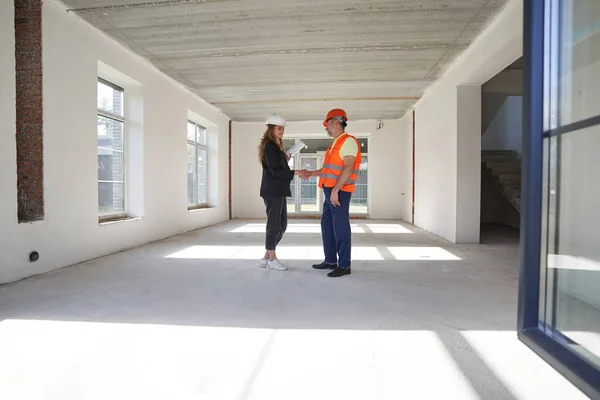 Nöjd kvinna designer ger handslag till byggarbetare inomhus — Stockfoto