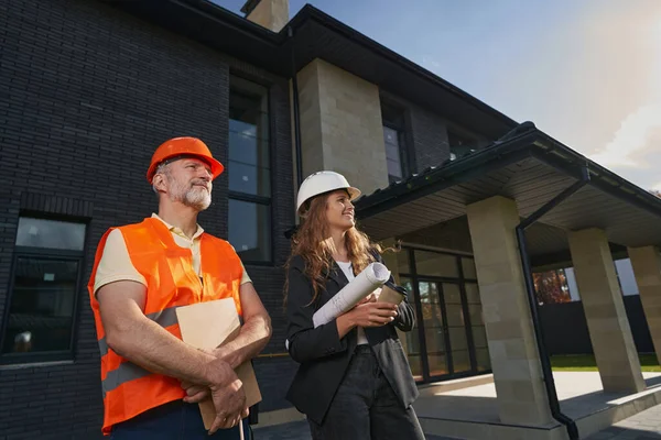 Pleased builder and woman engineer standing before house — Stockfoto