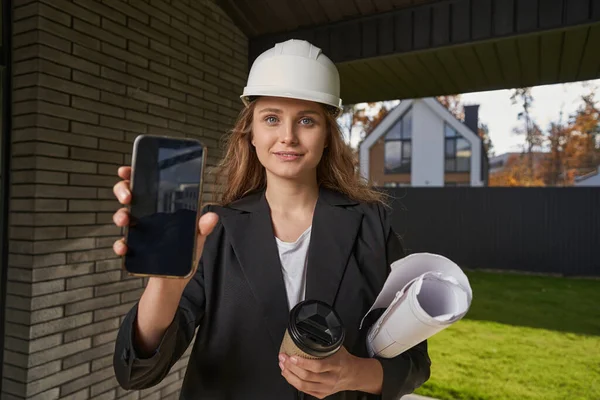 Ung kvinna utomhus visar telefon skärm till kamera — Stockfoto