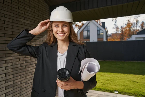 Kvinnlig ingenjör justerar sin hjälm nära husets ingång — Stockfoto