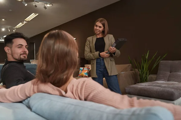 Pleased salesperson looking at shoppers in showroom — Stock Photo, Image