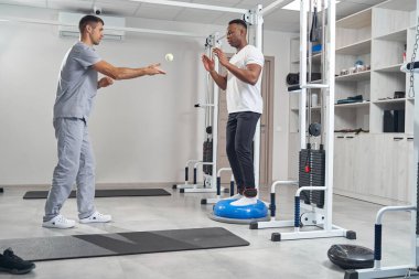 Ayak bileği ağırlıklı bir adam denge antrenörüyle çalışıyor.