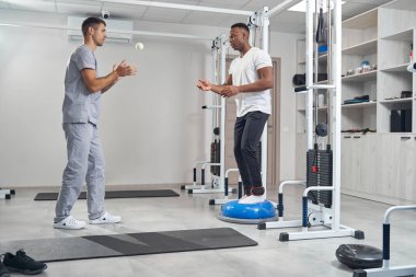 Ayak bileği ağırlıklı bir erkek denge antrenörü üzerinde egzersiz yapıyor.