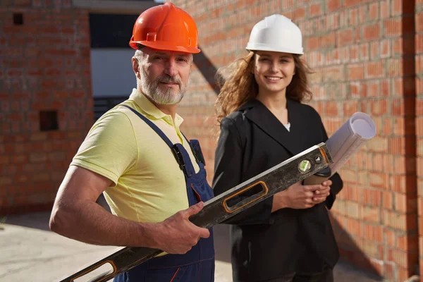 Man with spirit level looking at camera with female engineer — Stockfoto