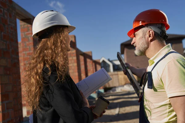 Stavitel domu se dívá na ženské stavební inženýr a ukazuje s úrovní — Stock fotografie