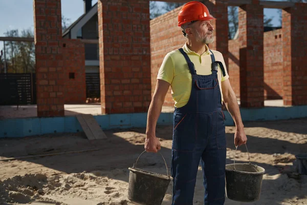 Byggherre med två skopor med sand på byggarbetsplatsen — Stockfoto