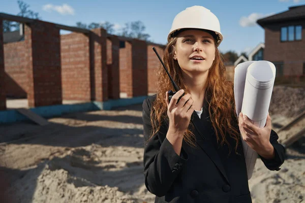 Female engineer with blueprint talking into walkie-talkie — 图库照片