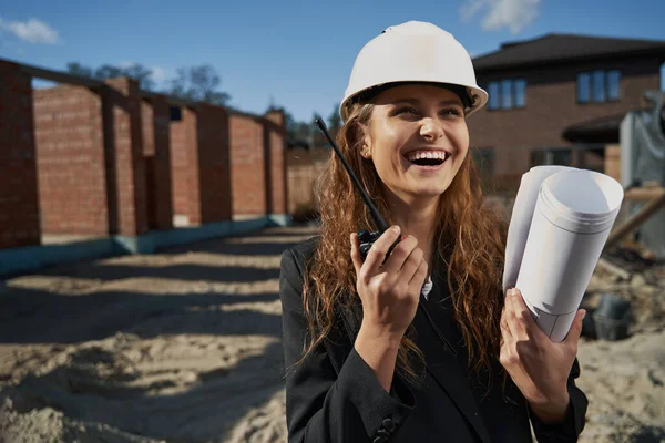 Lachende vrouw werknemer met lay-out praten door radio — Stockfoto