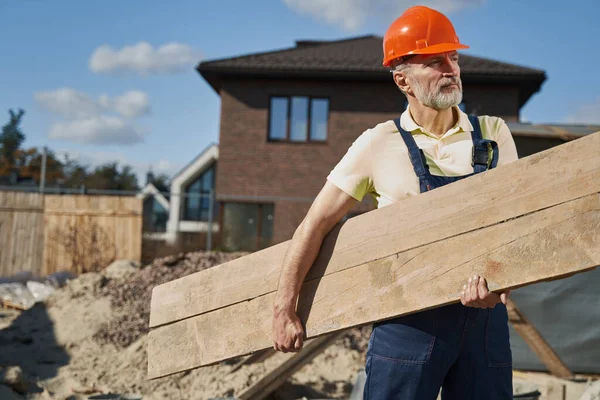 Äldre arbetstagare som går igenom byggarbetsplatsen med träplanka — Stockfoto