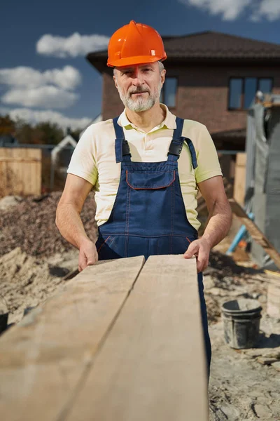 Senior builder stretching out board to camera — Stockfoto