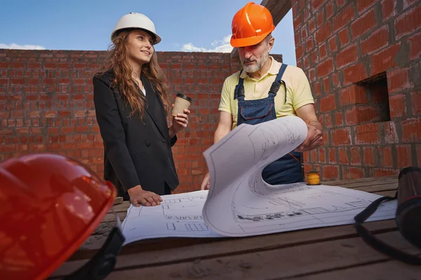 Vrouw ingenieur op zoek naar kant, terwijl de werknemer bestudeert blauwdrukken — Stockfoto