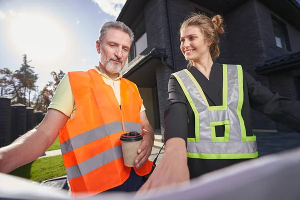 Satisfied construction engineer pointing out something on drawings to worker — Stockfoto
