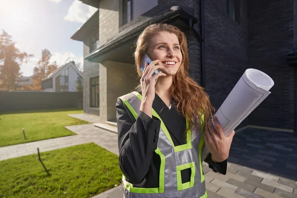 Excited woman site engineer with drawings talking on phone — Stockfoto
