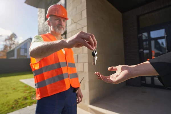 Person som tar nycklar från byggnadsarbetare utomhus — Stockfoto