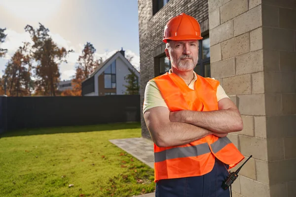 Allvarlig manlig byggare poserar för kamera nära huset — Stockfoto