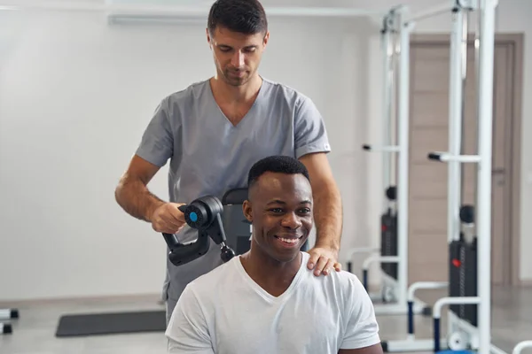 Fysiotherapeut met behulp van percussieve therapie apparaat op jonge man — Stockfoto