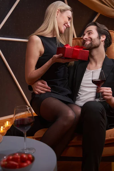 Żywa kobieta siedząca na męskim kolanie z prezentem i uśmiechnięta — Zdjęcie stockowe