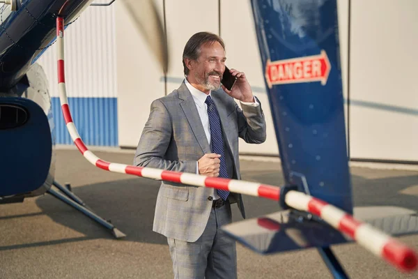 Joyous businessman talking on smartphone beside rotorcraft — Stock fotografie