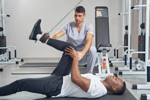 Чоловік виконує вправи на нозі під контролем фізіотерапевта — стокове фото