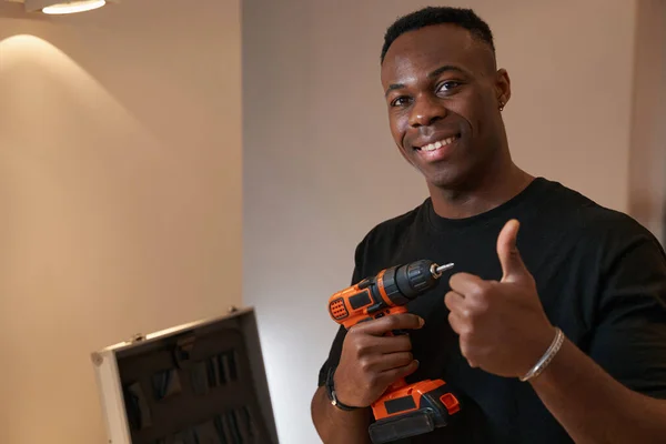 Multiracial man with drill showing thumbs-up to camera — Foto Stock