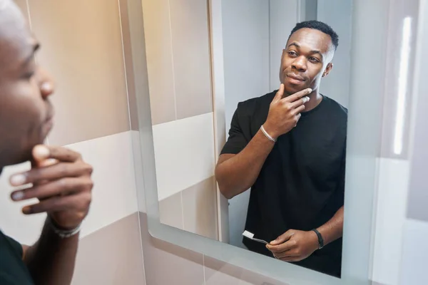 Multiethnic male studying his face in mirror of bathroom — Fotografia de Stock