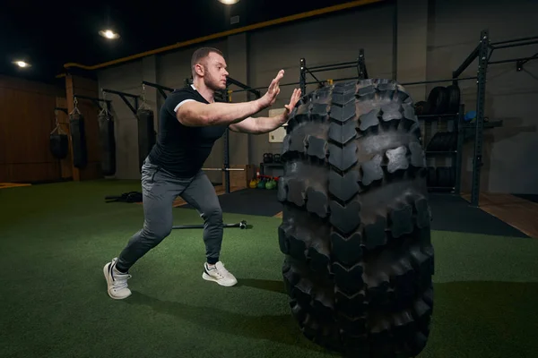 Sportsman doing tire flipping workout at gym