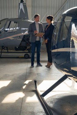 Metal hangarda bir erkekle konuşan şık bir kadın.