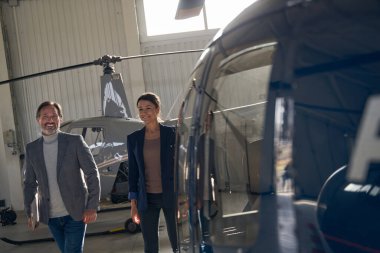İki neşeli insan hangarlı helikopterlerin yanından geçiyor.