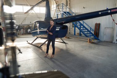 Kadın girişimci hangarlı helikopterin yanında duruyor.