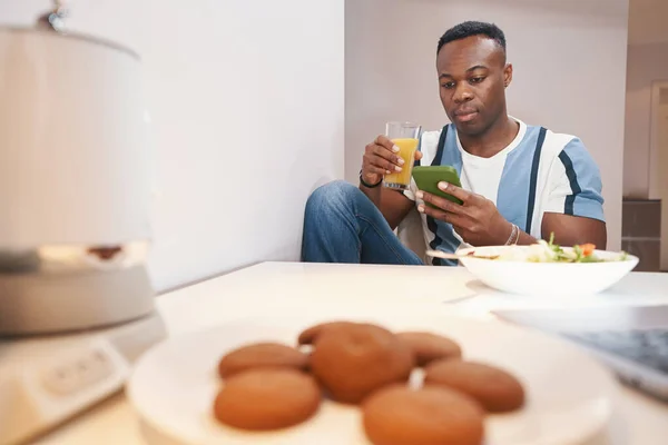 Hombre en casa beber jugo mientras se utiliza el teléfono inteligente —  Fotos de Stock