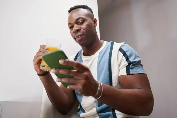 Hombre multiracial mirando el teléfono inteligente mientras bebe jugo —  Fotos de Stock