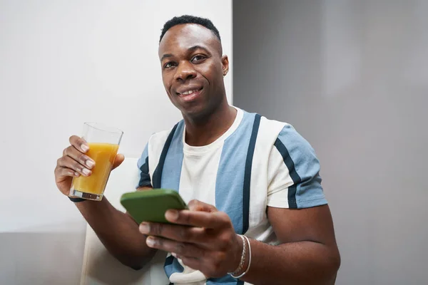 Feliz macho sosteniendo zumo de naranja y teléfono —  Fotos de Stock