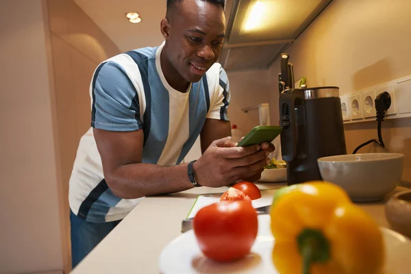 Man med smartphone lutar sig mot köksbordet — Stockfoto