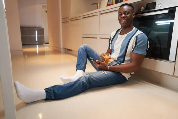 Jovem deitado no chão com smartphone na cozinha — Fotografia de Stock