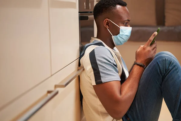 Männchen in Maske SMS am Telefon in der Küche — Stockfoto
