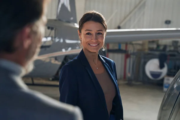 Alegre dama de pie ante el hombre en hangar de aviones — Foto de Stock