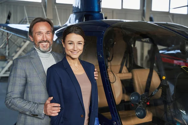 Glad gentleman och dam står bredvid helikopter i hangaren — Stockfoto