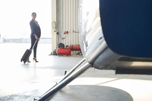 Doamnă elegantă cu valiză de cărucior în picioare în hangar de aeronave — Fotografie, imagine de stoc