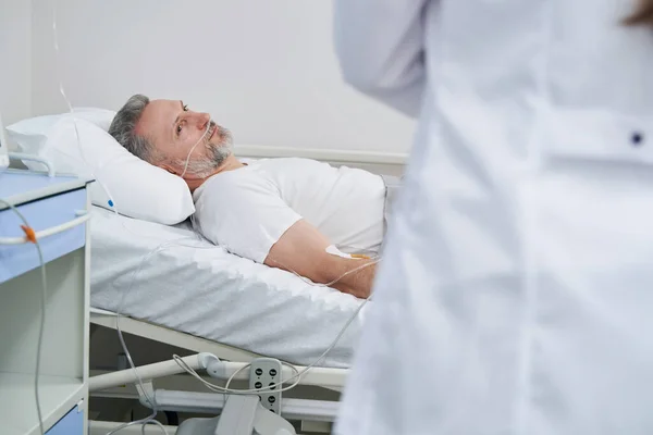 Liegender Patient starrt während Stationsrunde auf behandelnden Arzt — Stockfoto