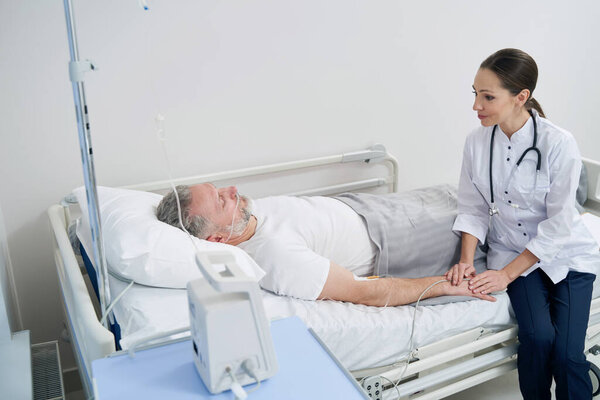 Опытный лечащий врач контролирует зрелого мужчину на внутривенной терапии