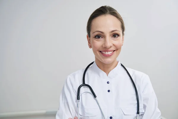 Freudiger junger Arzt posiert für Kamera am Arbeitsplatz — Stockfoto