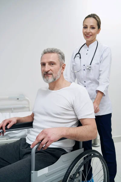 Fisioterapeuta sonriente y su paciente masculino posando para la cámara — Foto de Stock