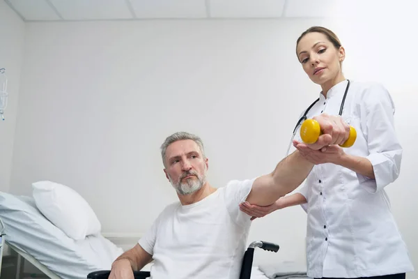 Paciente en silla de ruedas que realiza ejercicio en el brazo asistido por médico — Foto de Stock