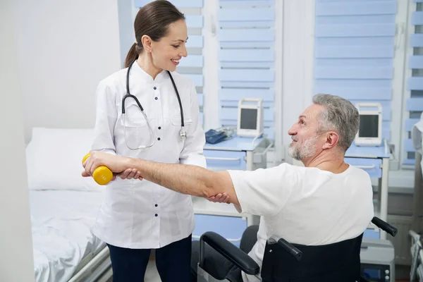 Mannelijke patiënt tillen van de hand gewicht bijgestaan door vriendelijke fysioloog — Stockfoto