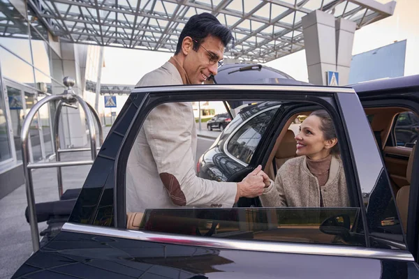Hombre en gafas tomando la mano de la mujer mientras ella sale del coche — Foto de Stock