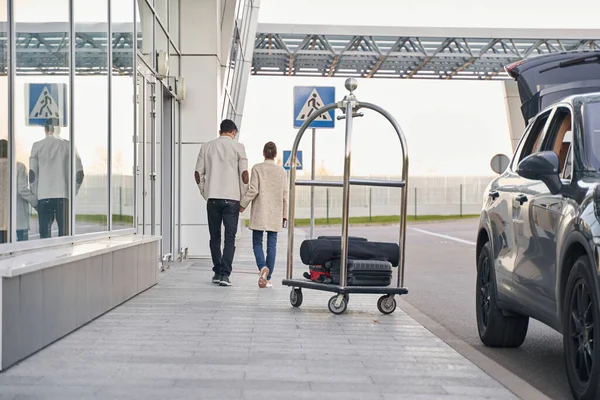 Пара, що ходить по будівлі аеропорту перед багажним візком — стокове фото