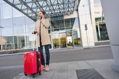 Bavulunun yanında otururken telefona cevap veren heyecanlı bayan.